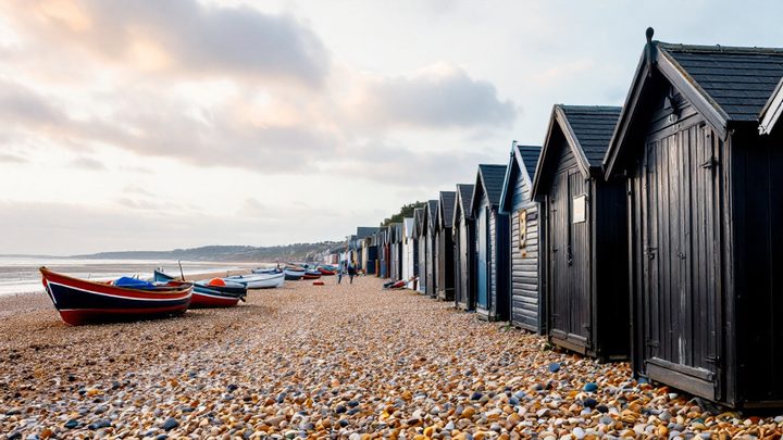 A shingle beach with tall black wooden net huts and fishing boats on the shore